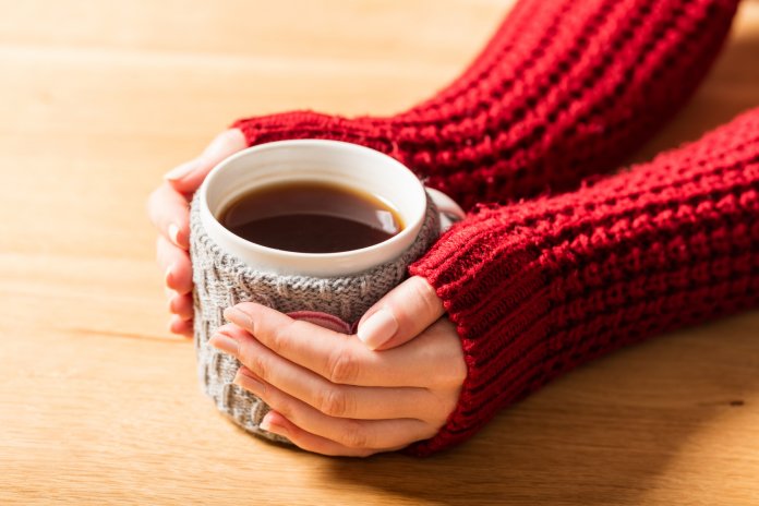 Hot mug of tea warming woman's hands in retro jumper.