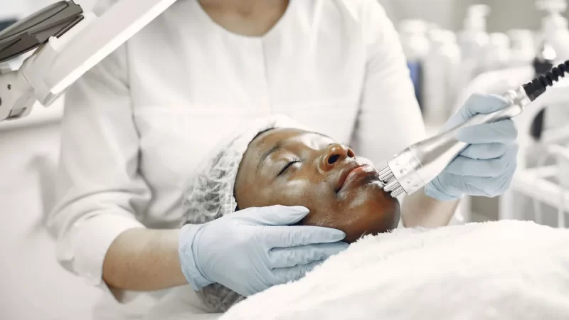 Dermatolog wykonuje zabieg na twarzy pacjentki specjalistycznym urządzeniem.
